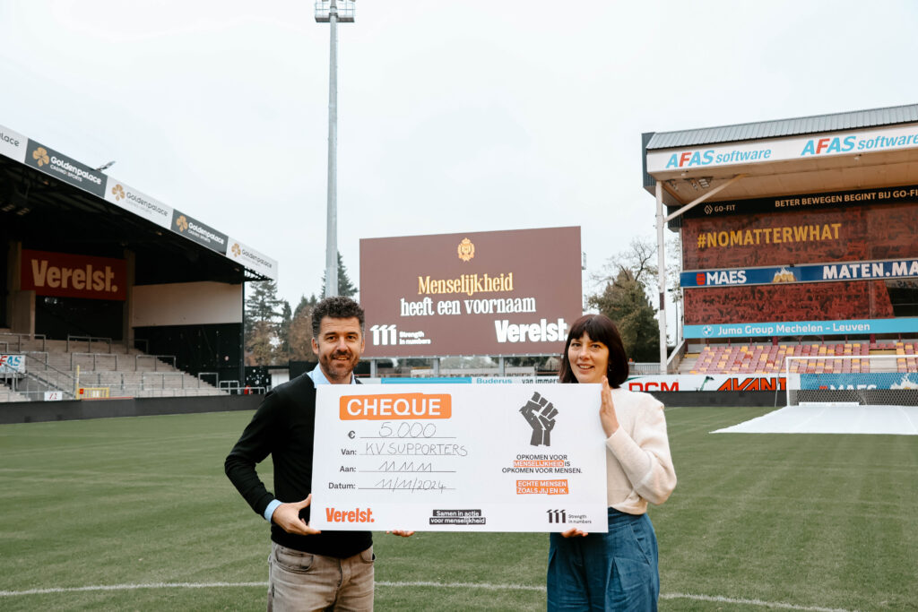 Stijn Dom van Verelst en Els Hertogen van 11.11.11 met de cheque op het veld van KV Mechelen.